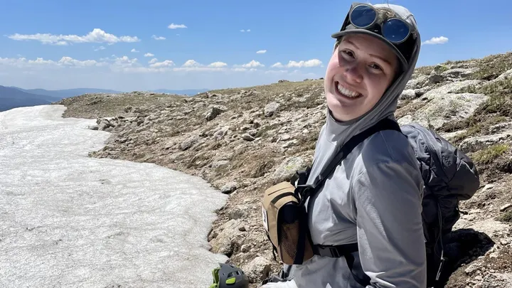 NMSU doctoral student Whitney Watson sits on a rocky mountainside near a snowfield during field research at Vermejo Park Ranch.