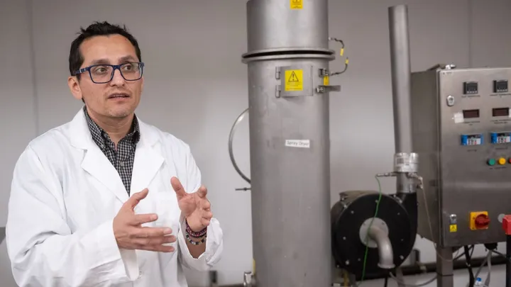 New Mexico State University researcher Sergio Martinez-Monteagudo gestures while standing beside food-processing equipment in a campus laboratory.