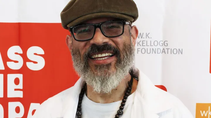 Manuel González, host of the “Pass the Sopapillas” podcast and New Mexico state poet laureate, smiles while standing in front of a W.K. Kellogg Foundation and “Pass the Sopapillas” backdrop.