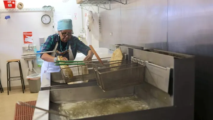 A kitchen worker places food into a deep fryer in a commercial kitchen during food preparation.