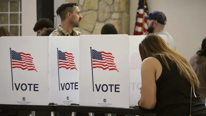 A woman casts a ballot at a voting booth while other voters stand inside a polling location in Doña Ana County.