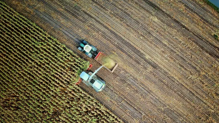 An aerial view shows farm equipment harvesting crops in a large agricultural field.