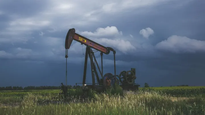 Oil pumpjack operating in a grassy field beneath dark storm clouds.