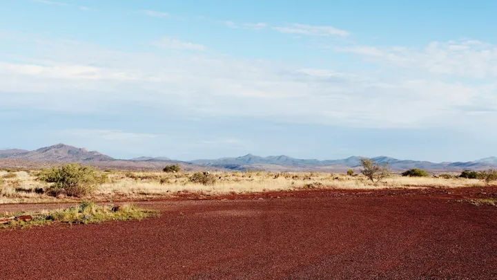 Dry New Mexico desert landscape with sparse vegetation, reddish soil and mountain ranges under a partly cloudy sky.