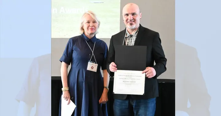 Dr. Jerry Wallace holds a state heritage preservation award while standing beside Audra Bellmore during an awards ceremony.