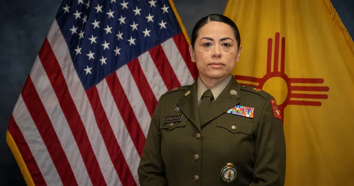 Master Sgt. Melissa Gonzales stands in uniform in front of the U.S. and New Mexico flags.