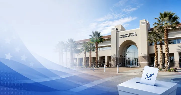 Election-themed illustration of the Doña Ana County Government Center with a ballot box graphic in the foreground and blue civic design elements.