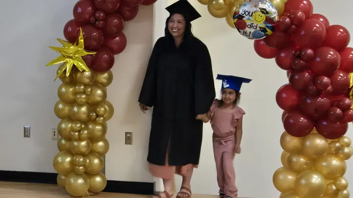 Maria Durado walks with her child under a red and gold balloon arch during an AVANCE to College graduation celebration.