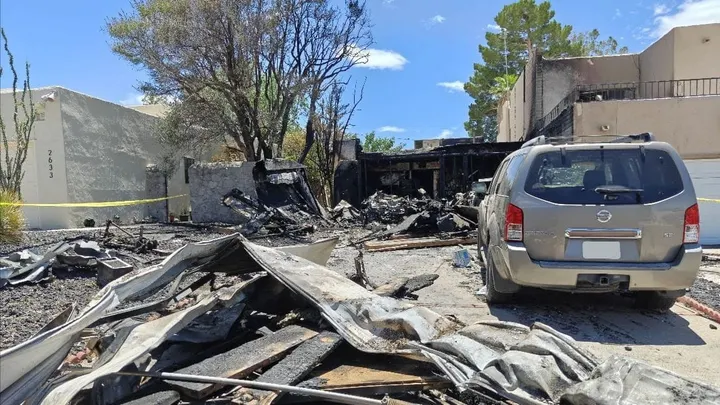 Fire and explosion damage outside a Fairway Drive residence in Las Cruces, with burned debris, a scorched garage area and a damaged SUV in the driveway.