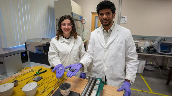 A professor and student hold scrap metal parts in a lab where they melt and reuse the metal.