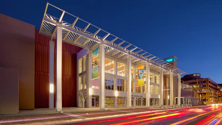 The Albuquerque Convention Center stands in downtown Albuquerque with trees, streetlights and surrounding buildings visible.