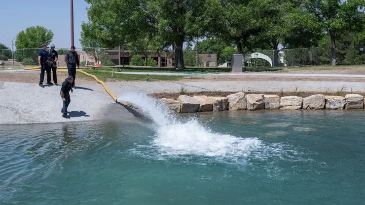 Three workers monitor a hose discharging water into the renovated Alumni Pond at New Mexico State University.