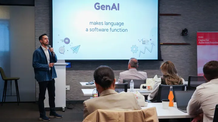 A presenter speaks into a microphone during a GenAI workshop while attendees watch a projected slide about language and software.