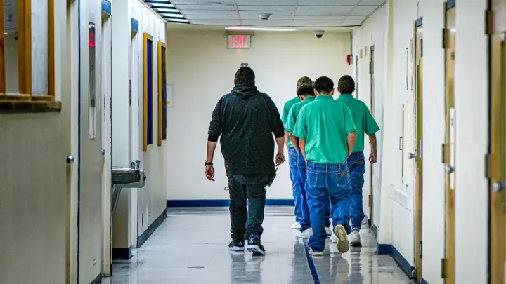 A staff member walks with a group of boys in green shirts through a hallway at the Youth Diagnostic and Development Center.