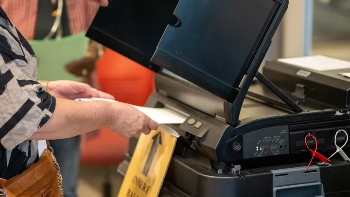 A voter feeds a ballot into an election tabulator.