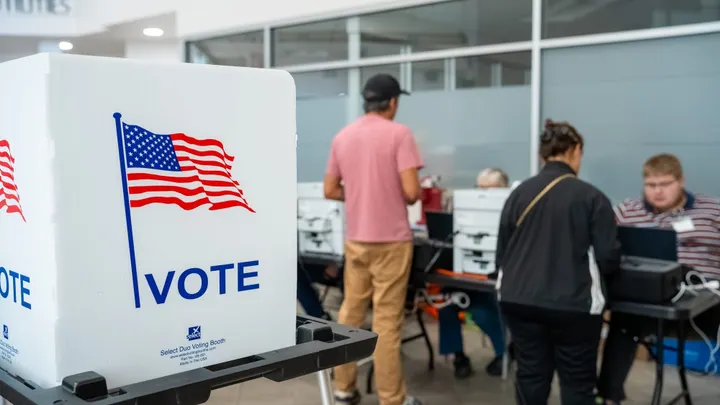 A voting booth stands in the foreground as people check in at a polling location in Doña Ana County.