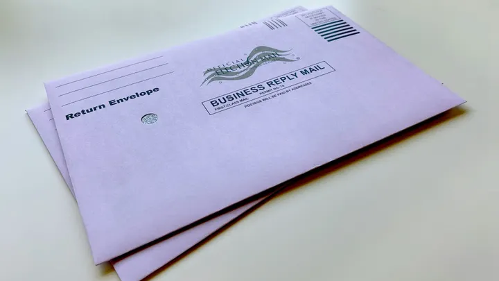 Mail-ballot return envelopes sit on a light-colored surface.