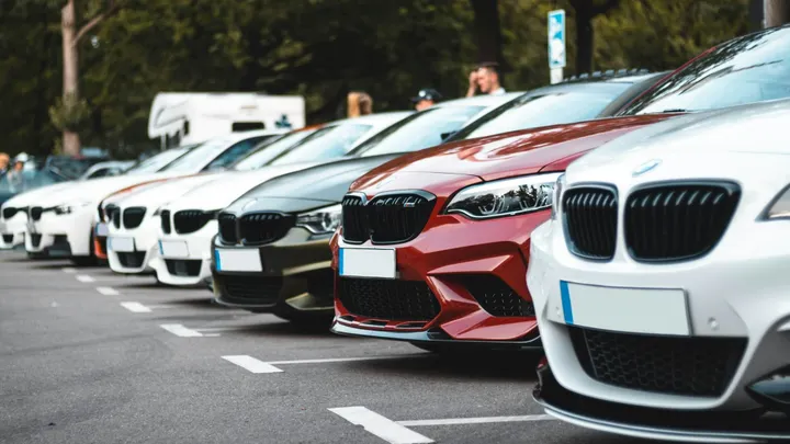 A row of parked vehicles is shown in a parking lot, led by white and red cars in the foreground.