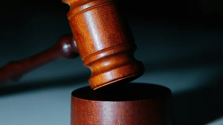 Wooden judge’s gavel positioned above a sound block against a dark background.