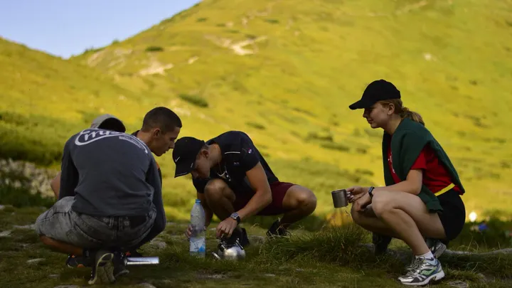 Young people crouch in a grassy mountain area during an outdoor conservation program.