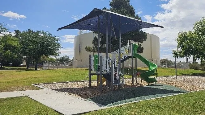 A shaded playground with a green slide sits on rubberized surfacing at Gus Vlachakis Park in Las Cruces.