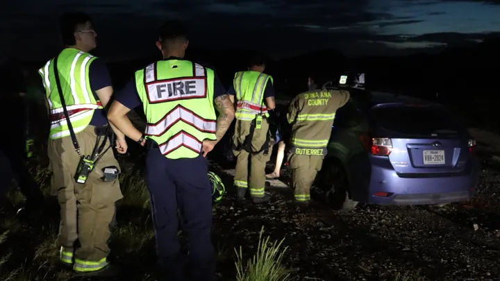 Doña Ana Fire Rescue crews stand near a damaged vehicle at night after a crash near Highway 404 in Chaparral.
