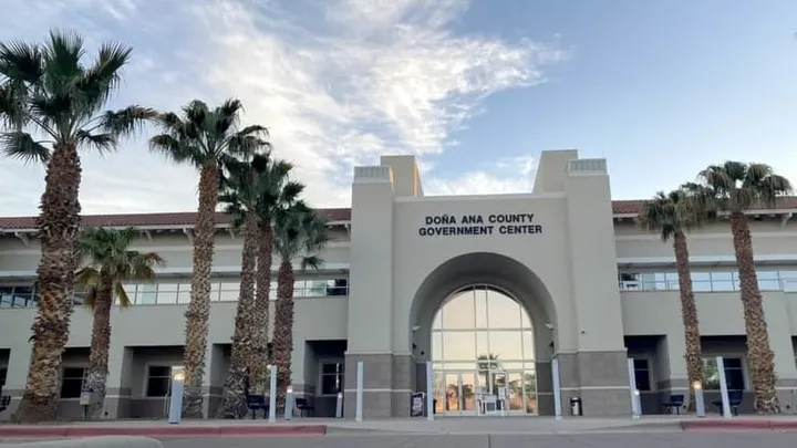 The entrance to the Doña Ana County Government Center is shown with palm trees in front of the building.