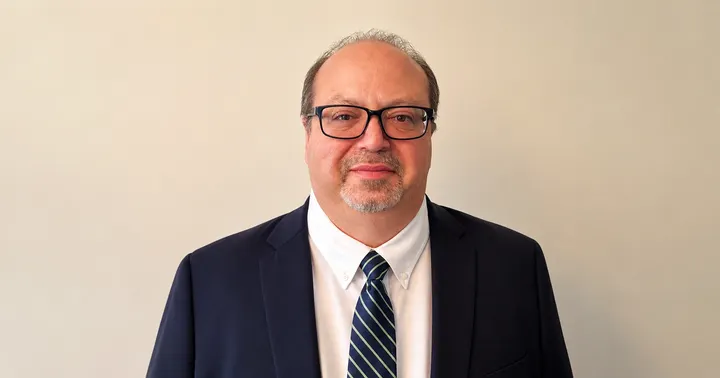 Michael Pullin poses for a portrait wearing glasses, a dark suit jacket and a striped tie.