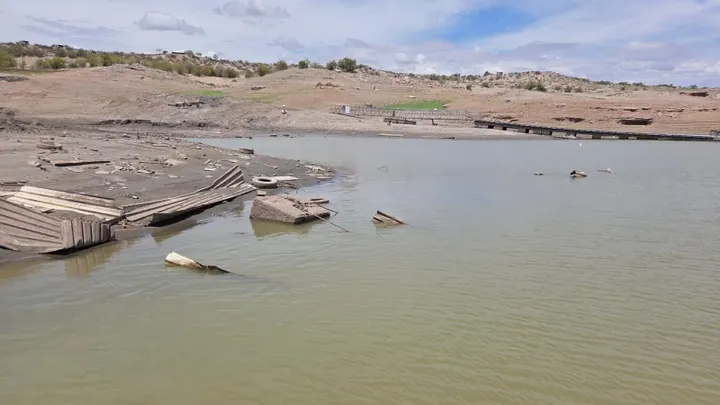 Exposed debris and a partially submerged boat ramp are visible along the receding shoreline at Elephant Butte Lake.