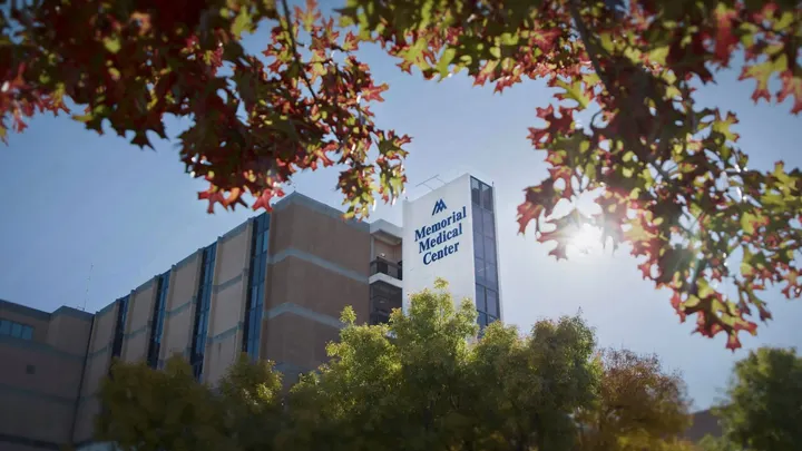 Memorial Medical Center is shown in Las Cruces with tree branches and sunlight in the foreground.