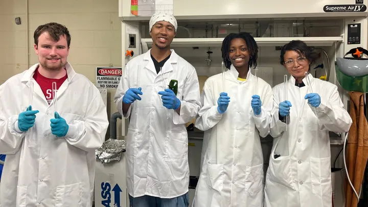 Four students in NMSU’s NuChemE Pipeline summer program hold test tubes while standing in a laboratory.