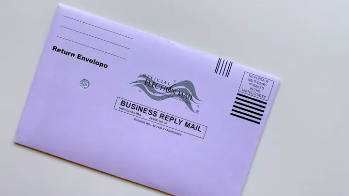 An official election mail return envelope sits on a table.
