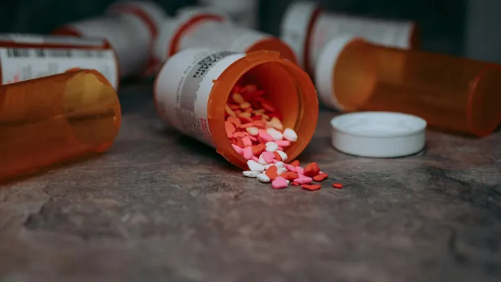 Orange prescription bottles scattered on a table, with multicolored pills spilling from one open container.