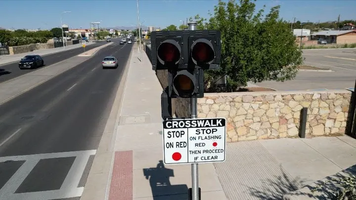 A HAWK pedestrian crossing signal and crosswalk stand beside W. Amador Avenue in Las Cruces, with traffic moving along the multi-lane roadway.