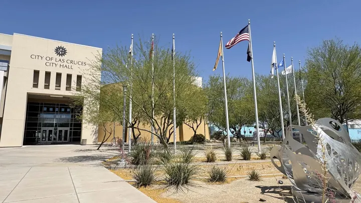 Exterior of Las Cruces City Hall with flags, desert landscaping and public art in front of the building.