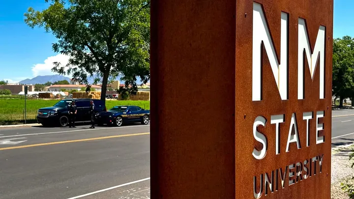 Las Cruces and NMSU police vehicles are parked along University Avenue near a New Mexico State University sign during a traffic enforcement operation.