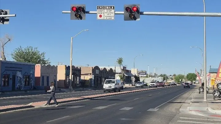 A pedestrian crosses a wide Las Cruces roadway beneath red crosswalk signals as vehicles travel through the surrounding lanes.