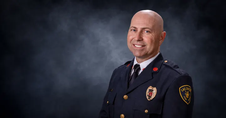 Las Cruces Fire Department Deputy Chief Justin Whitefield poses in uniform against a dark blue-gray studio background.
