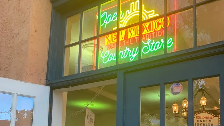 Entrance to the New Mexico Country Store at the State Fair, with a brightly lit neon sign above blue doors.