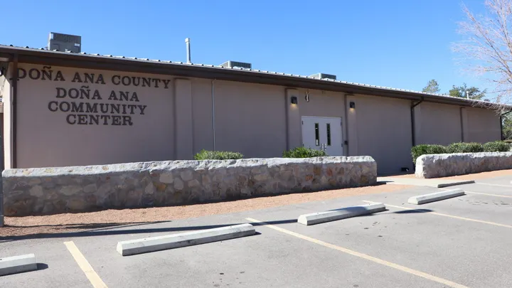 Exterior of the Doña Ana Community Center, with the facility name displayed on the building above a stone-lined parking area.
