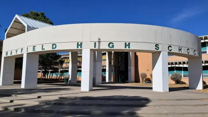 Exterior entrance to Mayfield High School in Las Cruces, with the school name displayed across a curved white facade under a clear blue sky.