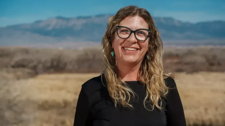 Laura Paskus smiles outdoors with a New Mexico landscape and mountains in the background.