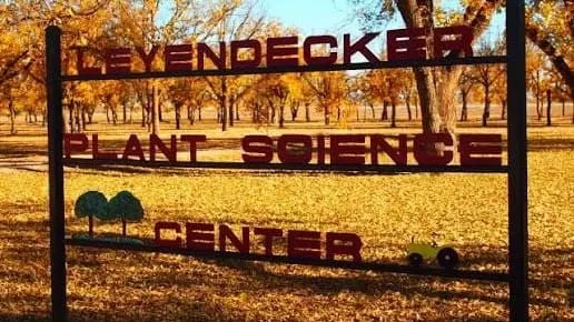 Sign for New Mexico State University’s Leyendecker Plant Science Research Center surrounded by trees with autumn foliage.