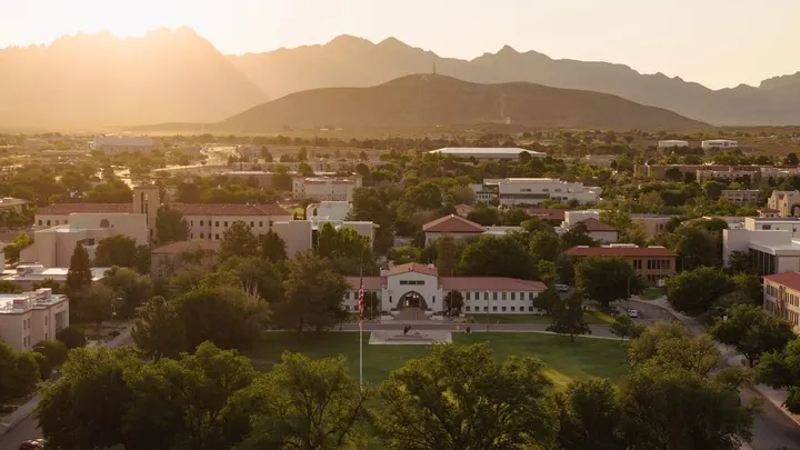 Aerial view of Hadley Hall and surrounding New Mexico State University campus buildings in Las Cruces, with the Organ Mountains visible at sunset.