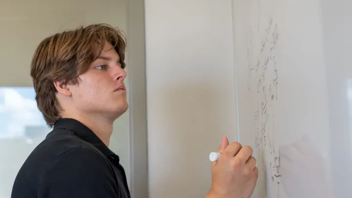 NMSU mechanical engineering student Quinn Thompson writes an equation on a whiteboard at the engineering tutoring center.