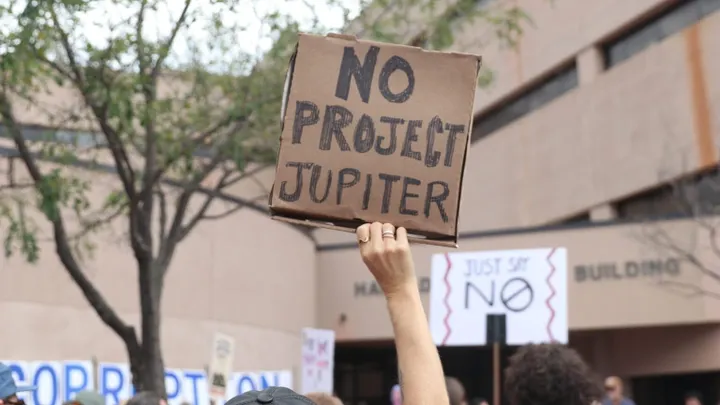 A protester holds a cardboard sign reading “NO PROJECT JUPITER” outside the New Mexico Environment Department in Santa Fe.
