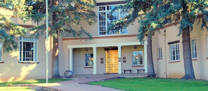 Exterior of the New Mexico Supreme Court building in Santa Fe, with trees framing the entrance and lawn.