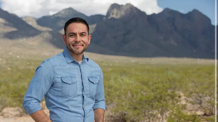 U.S. Rep. Gabe Vasquez stands outdoors in a blue shirt with the Organ Mountains rising behind him.