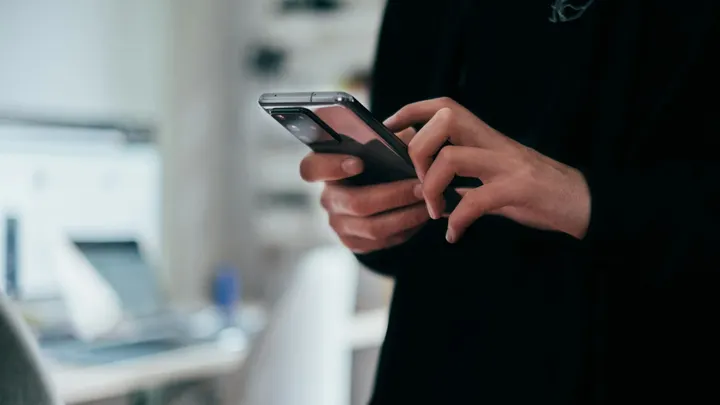 A person uses a smartphone indoors, holding the device in both hands and tapping the screen.