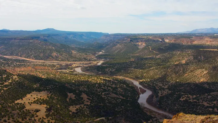 Aerial view of the Rio Grande winding through a broad, rugged landscape of mesas, arroyos and desert vegetation in New Mexico.